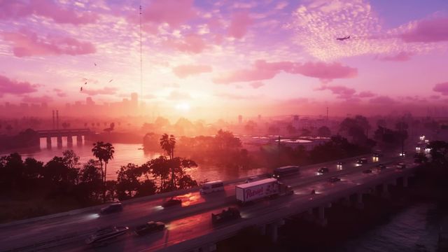 An aerial view captures a vibrant pink and purple sunrise or sunset over a city skyline with a multi-lane…