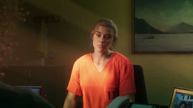 Lucia Caminos, wearing an orange prison jumpsuit, sits at a desk in an office with a painting of a boat on…