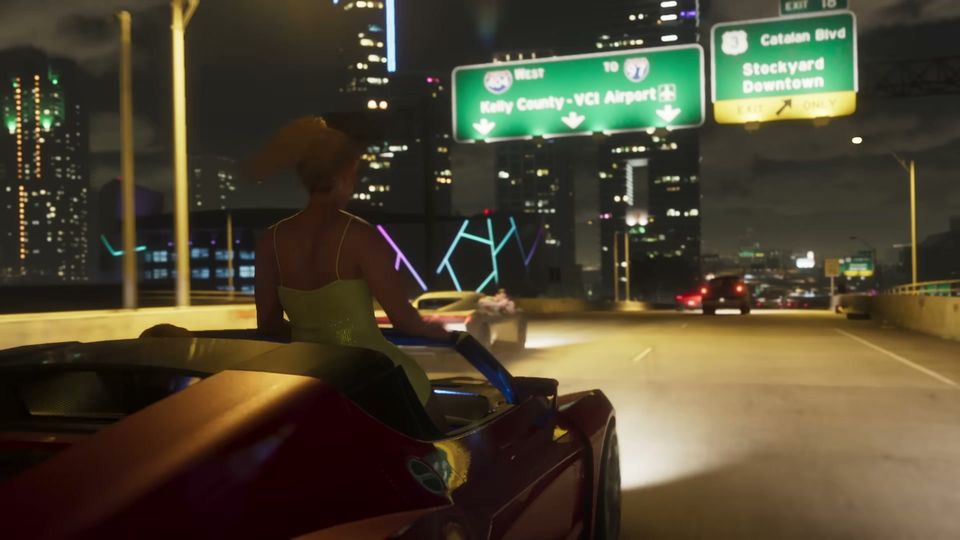 A woman with a ponytail is driving a red convertible car on a multi-lane highway at night, with a brightly lit city skyline and highway signs in the background.