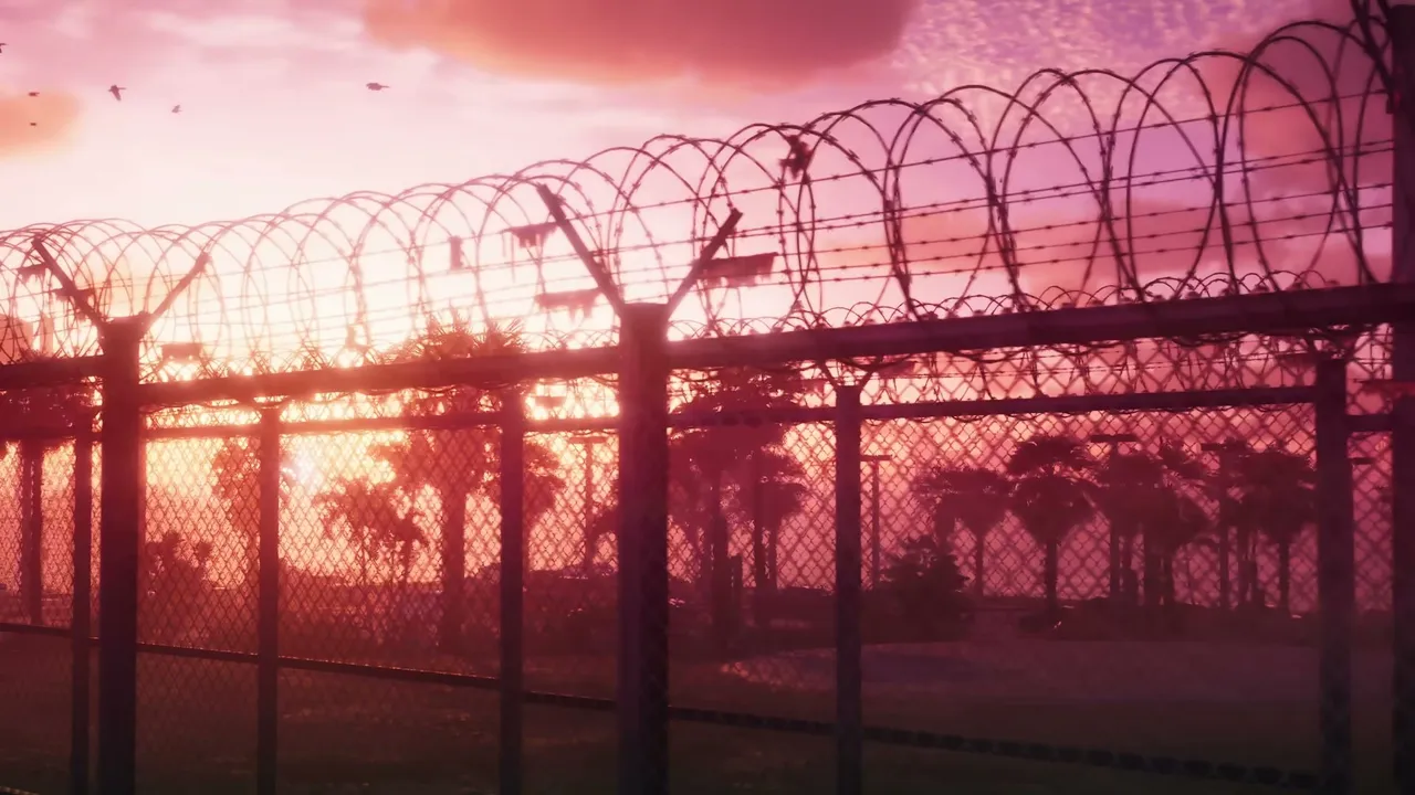 A chain-link fence topped with razor wire stands in the foreground, silhouetting palm trees and…