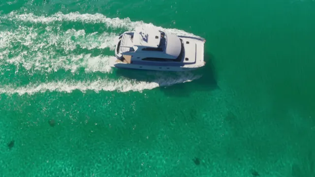 A white yacht is seen from an aerial perspective, cruising through clear turquoise water and leaving a white…