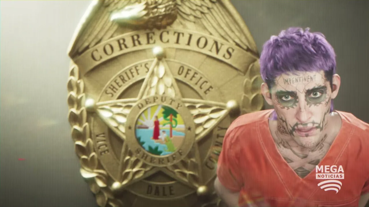 A man with purple hair, face tattoos, and an orange prison jumpsuit is shown in front of a large…