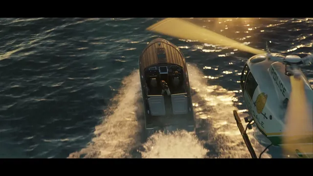 A police helicopter pursues a speedboat with two occupants over sun-dappled open water.